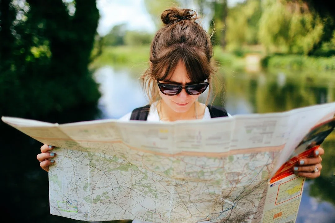 A person reading a folded paper map outdoors by the water