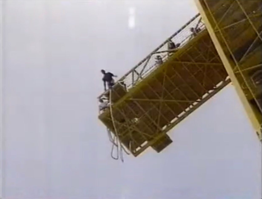 A figure at the edge of a high jump platform against an open sky